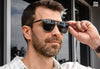 Man adjusting sunglasses outdoors, demonstrating eyewear style.