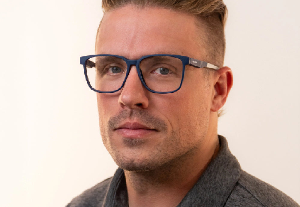 Close-up of a man wearing blue rectangular glasses against a neutral light background