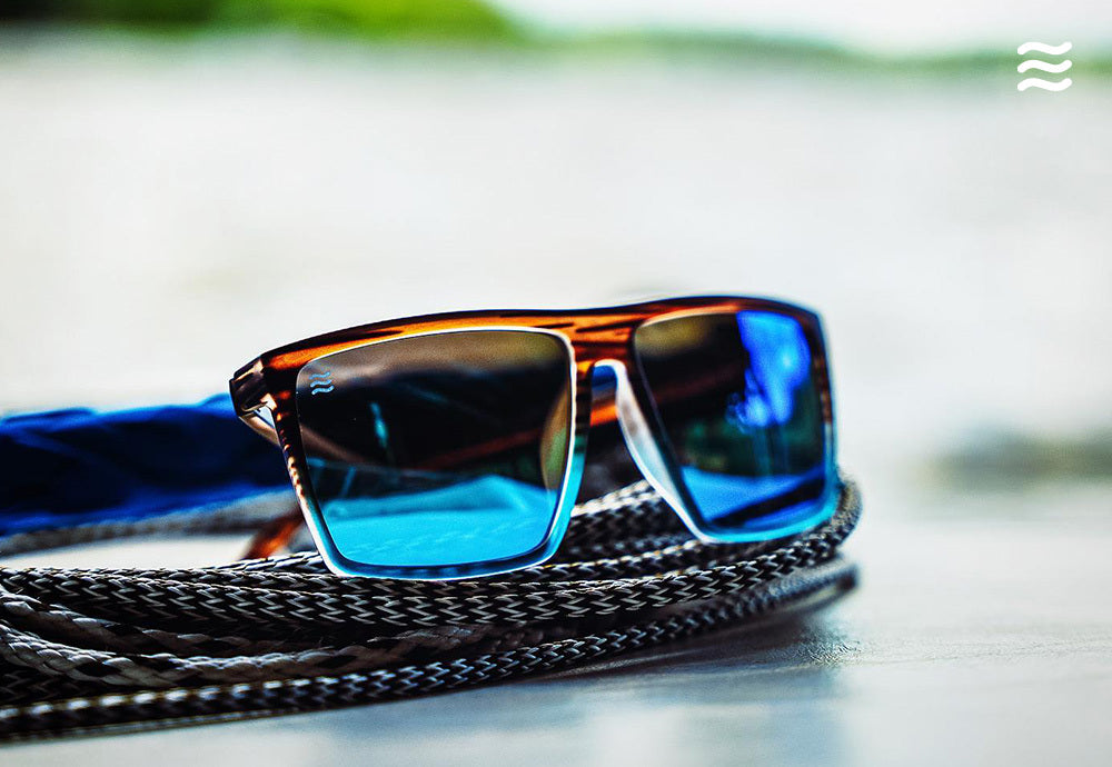 Close-up front three-quarter view of tortoiseshell sunglasses showcasing blue mirrored lenses resting on coiled rope