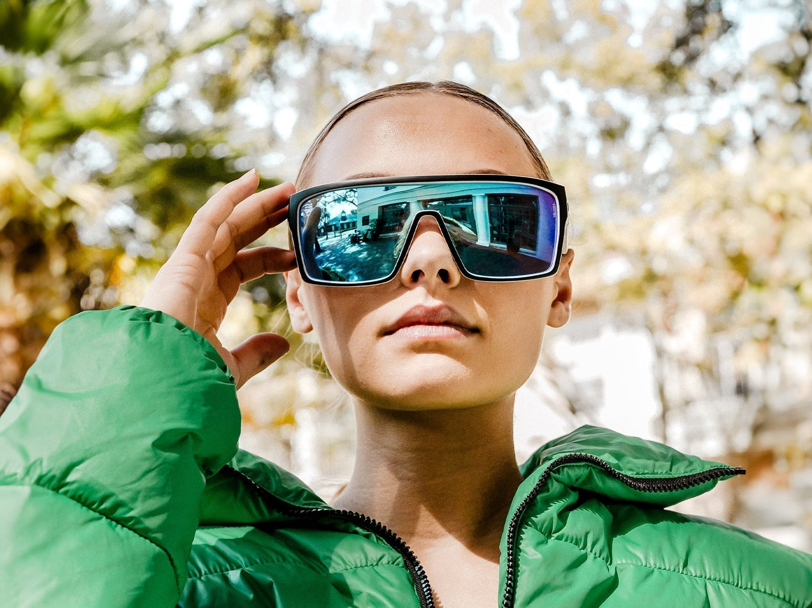 Close-up front view of oversized shield sunglasses with blue-green mirrored lenses and black frame on a model outdoors