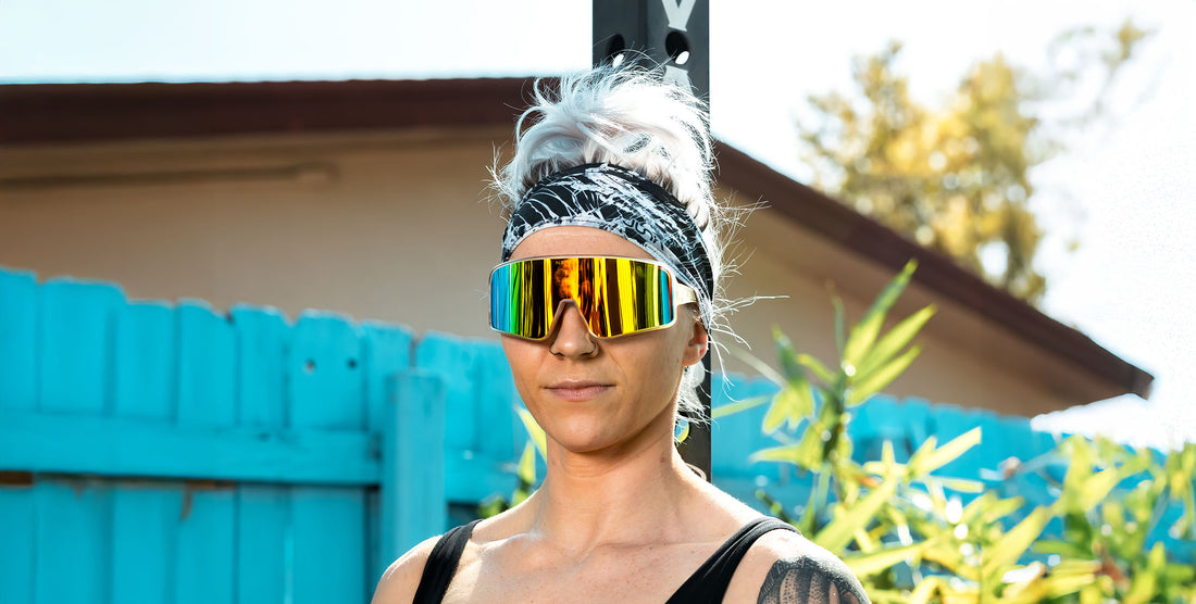 Front view of Energy sunglasses showcasing mirrored shield lenses with orange-green reflection against turquoise fence
