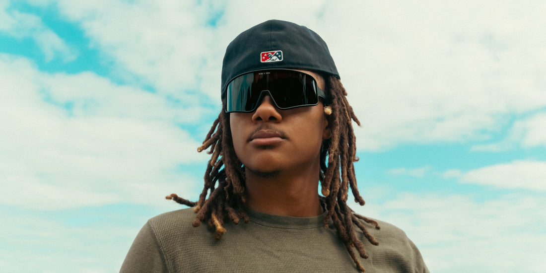 Front close-up of Resilience sunglasses showcasing a black polarized shield lens on a model with a cloudy blue sky background