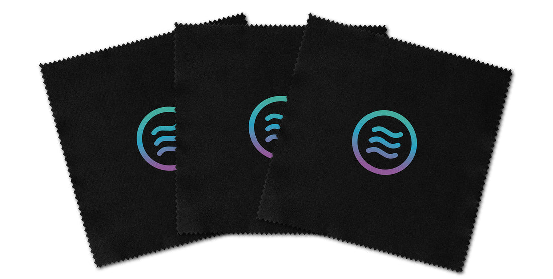 Overhead view of three microfiber lens cloths from 3-pack cleaning kit showcasing black non-abrasive fabric and teal-to-purple Neven tilde logo