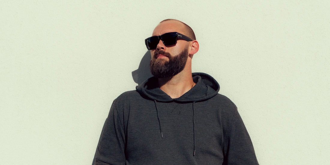 Man wearing Banshee sunglasses with black lenses against a pale green background
