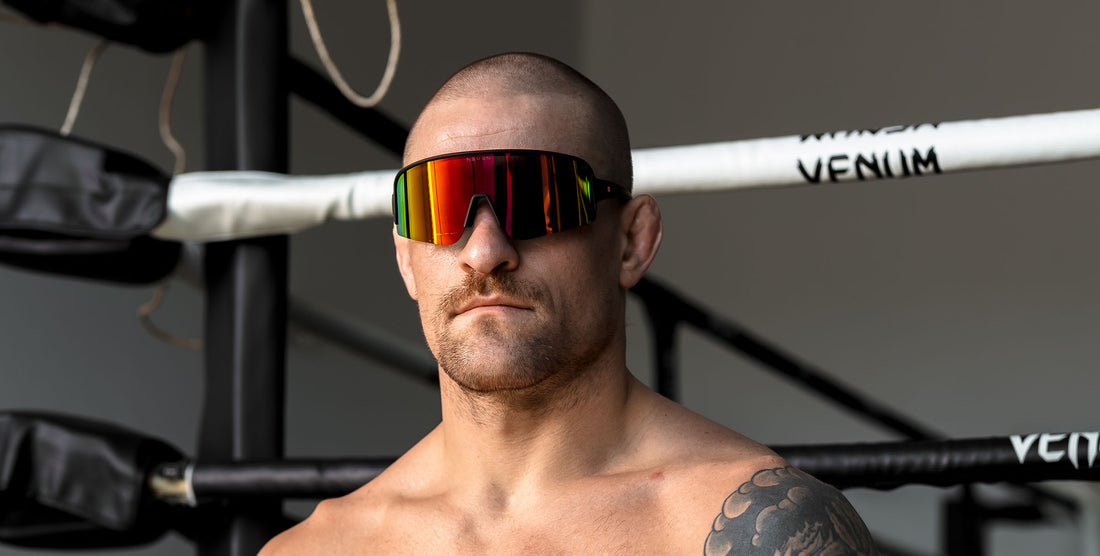 Man wearing black Cadence wraparound sunglasses with maroon reflective lenses in a boxing gym