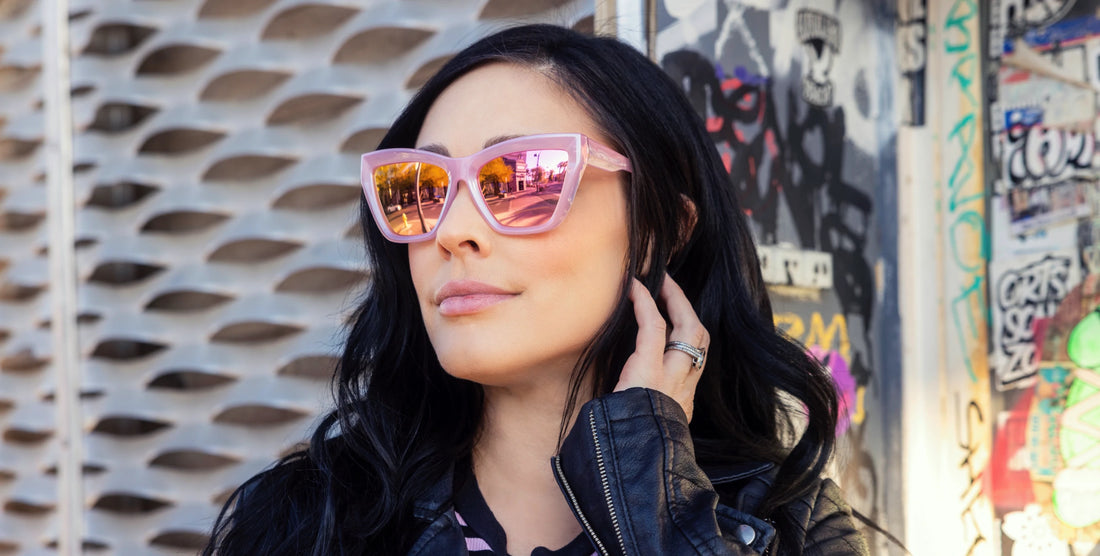 Woman wearing transparent pink Eclipse cat-eye sunglasses with mirrored polarized lenses, urban graffiti background