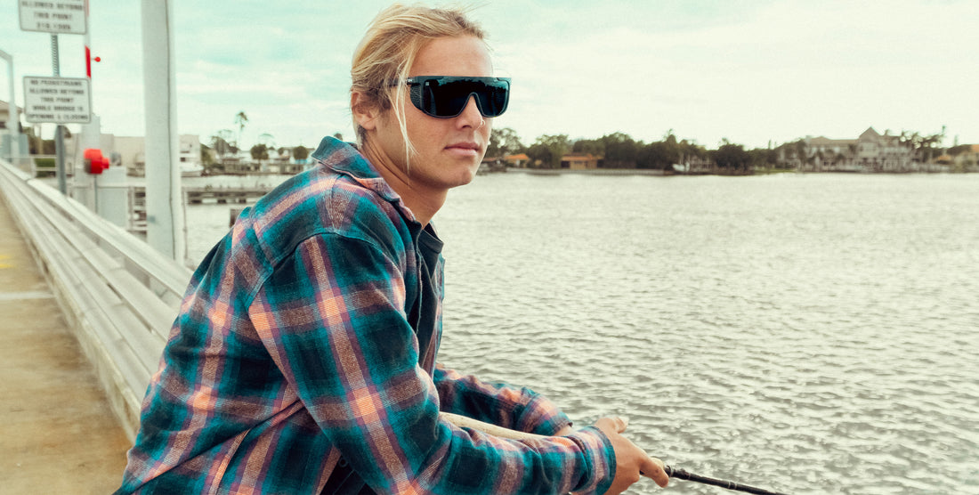 Young person wearing Pitch Black polarized sunglasses leaning on a pier by the waterfront