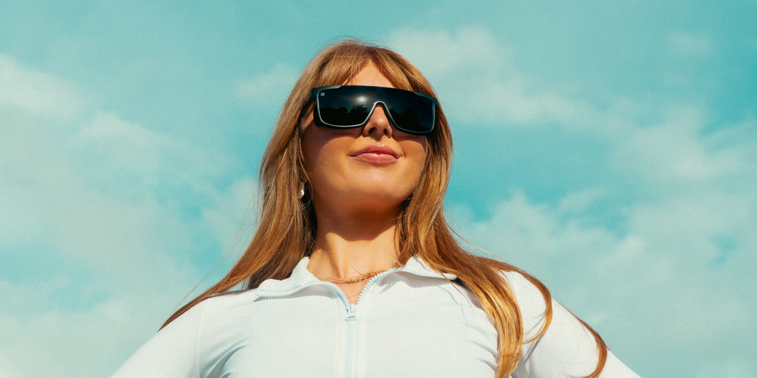 Woman wearing Pitch Black polarized sunglasses looking up against a blue sky