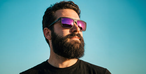 Close-up of 88th Street XL sunglasses with matte black X-Large frame and purple-pink polarized lenses against clear blue sky