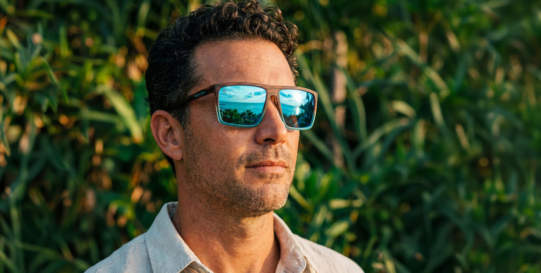 Man wearing Melby XL sunglasses outdoors, blue mirrored lenses reflecting ocean and wood-to-turquoise rectangular frame