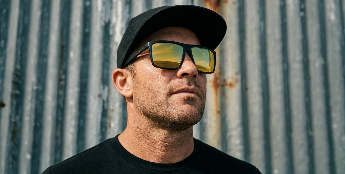 Man wearing a black cap and sunglasses against a corrugated metal background