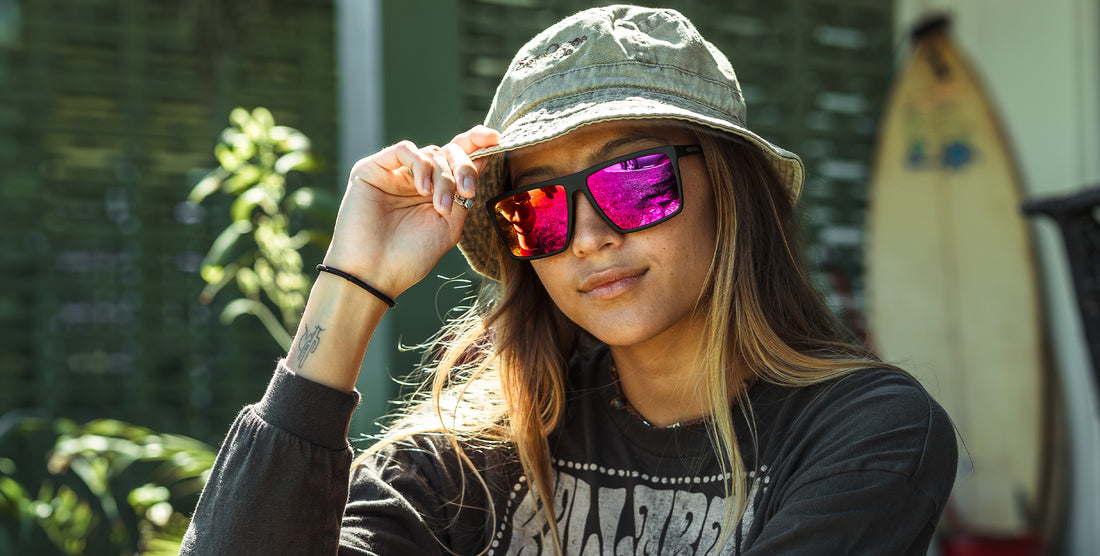 Three-quarter view of 88th Street sunglasses showcasing a matte black frame and polarized pink mirrored lenses on a woman wearing a bucket hat outdoors