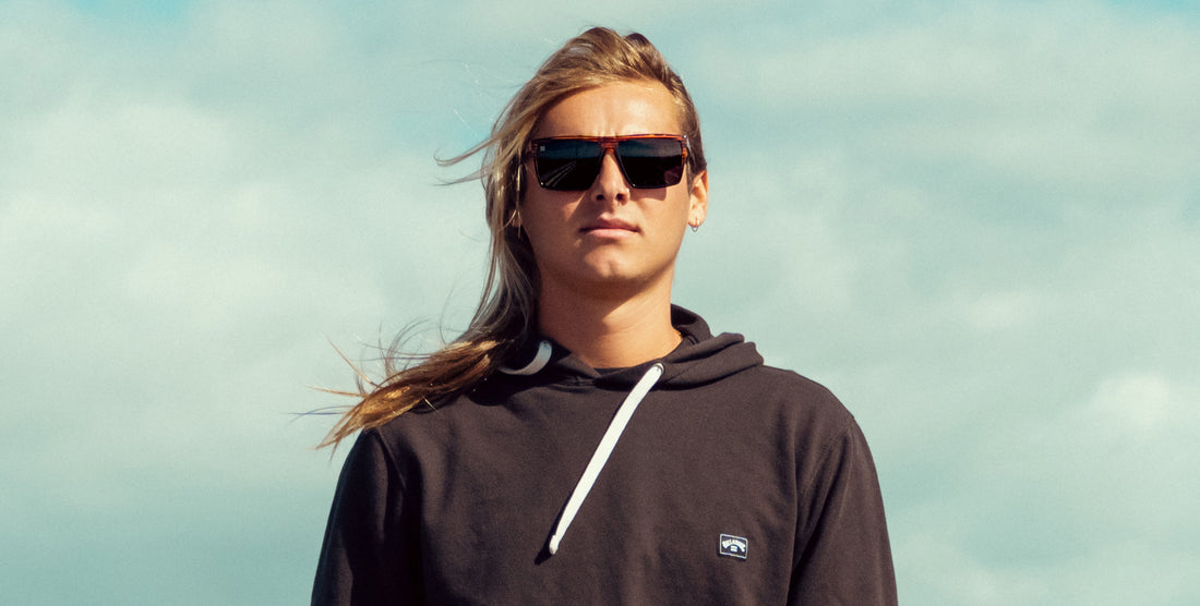 Front view of Asbury sunglasses showcasing black wood-grain rectangular frame and polarized black lenses on a model against a cloudy sky