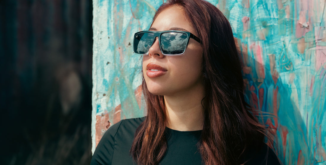 Woman wearing black rectangular Colorado Bulldog sunglasses against a colorful textured wall