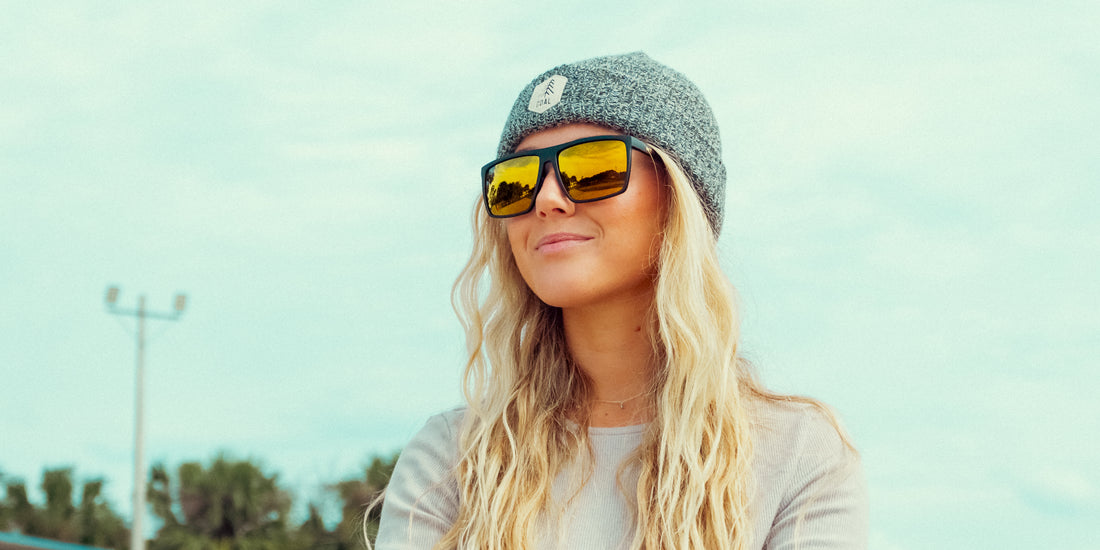 Woman wearing Norton sunglasses, smiling outdoors with black frames, yellow mirrored polarized lenses, and a gray knit beanie