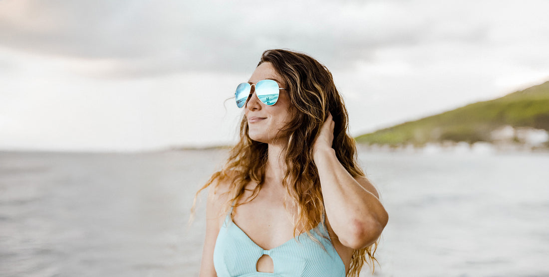 Woman wearing H2O stainless steel sunglasses with blue mirrored polarized lenses standing on a beach