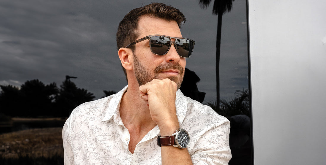 Man wearing Rip Tide transparent gray polarized sunglasses outdoors with palm trees in the background
