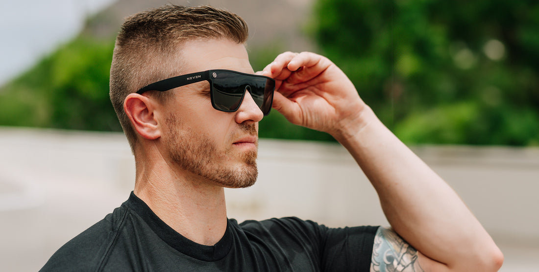 Man adjusting black Bold polarized sunglasses outdoors with greenery in the background