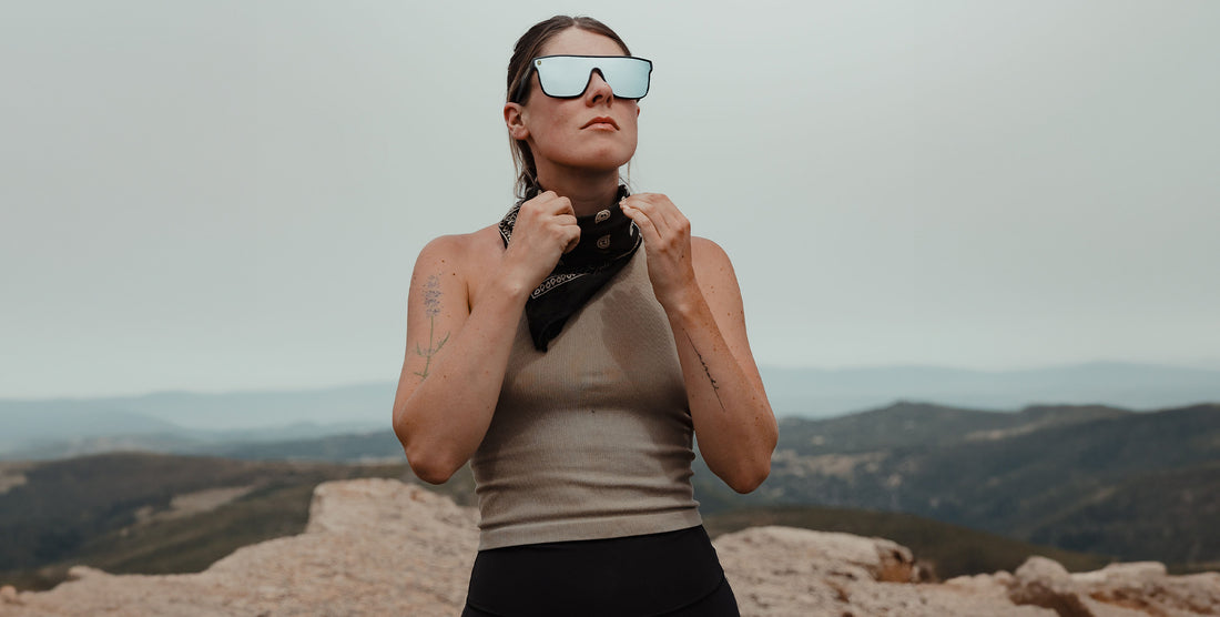 Woman wearing black CJ polarized sunglasses adjusts a neck scarf at a rocky mountain overlook