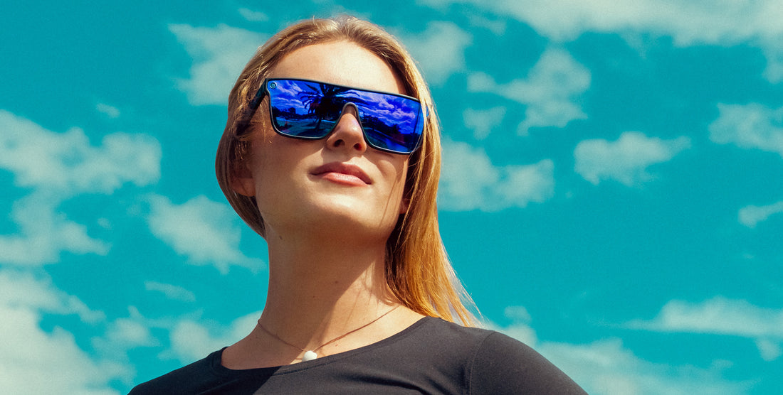Woman wearing Midnight blue polarized sunglasses with a black frame against a bright blue sky