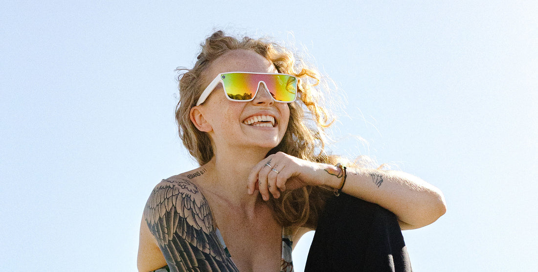 Smiling woman wearing white Muse sunglasses with pink and yellow lenses outdoors in bright sunlight