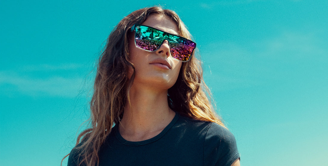 Woman wearing blue and purple polarized Nomads sunglasses against a bright blue sky