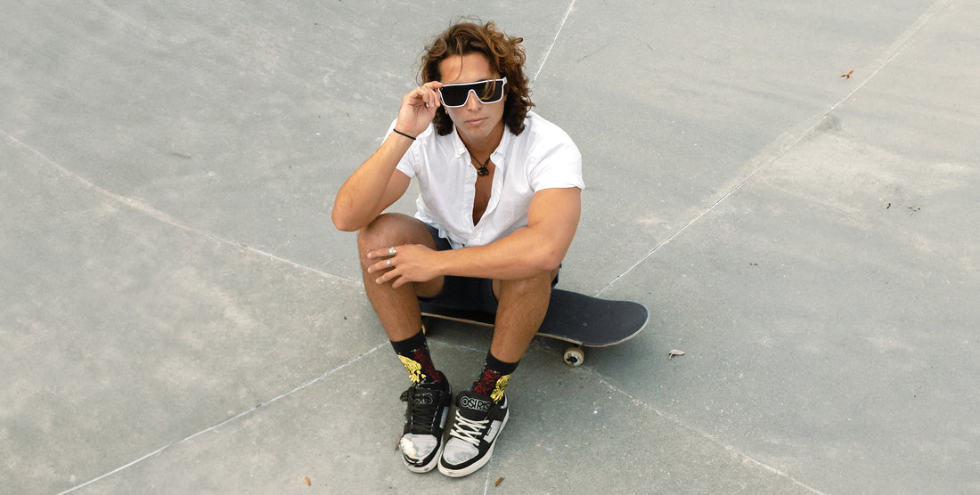Skateboarder sitting on a skateboard wearing white Permafrost XL polarized sunglasses at a concrete skatepark