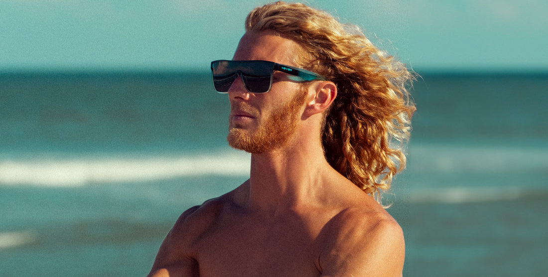 Man wearing Turnstile polarized sunglasses with black lenses and a black and blue frame by the ocean