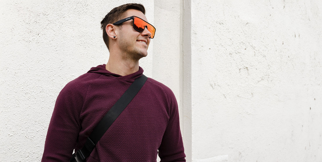 Man wearing Zero Cool sunglasses with orange polarized uni-lens smiling against a textured white wall