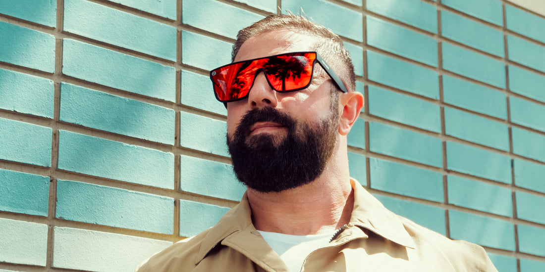 Man wearing Zero Cool XL oversized black sunglasses with red-orange mirrored polarized lenses standing against a turquoise tiled wall