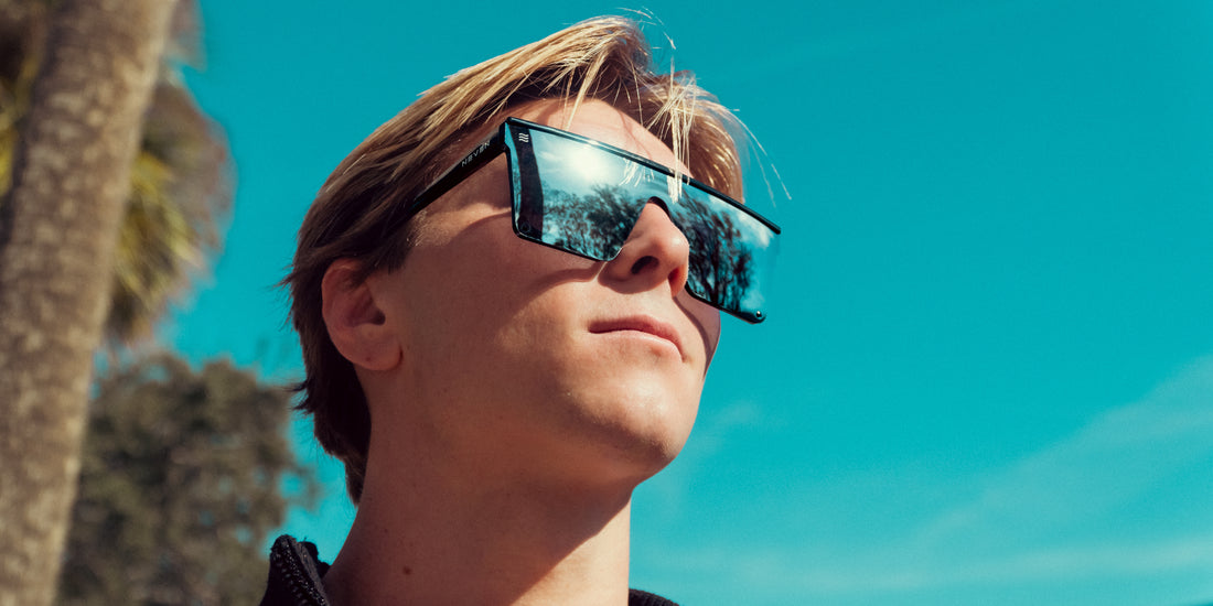 Model wearing Cr shield-shaped sunglasses with matte black frame and mirrored silver lenses against a bright blue sky