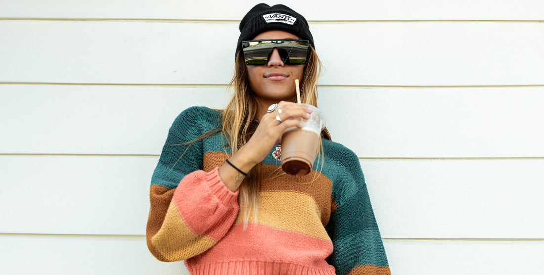 Woman wearing IWMSAN black angular polarized sunglasses sipping iced coffee in front of a white paneled wall
