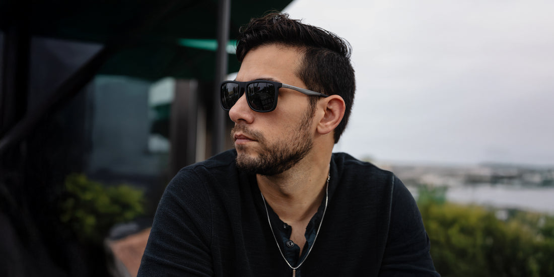 Man wearing black rectangular Blueprint polarized sunglasses outdoors with a blurred city view