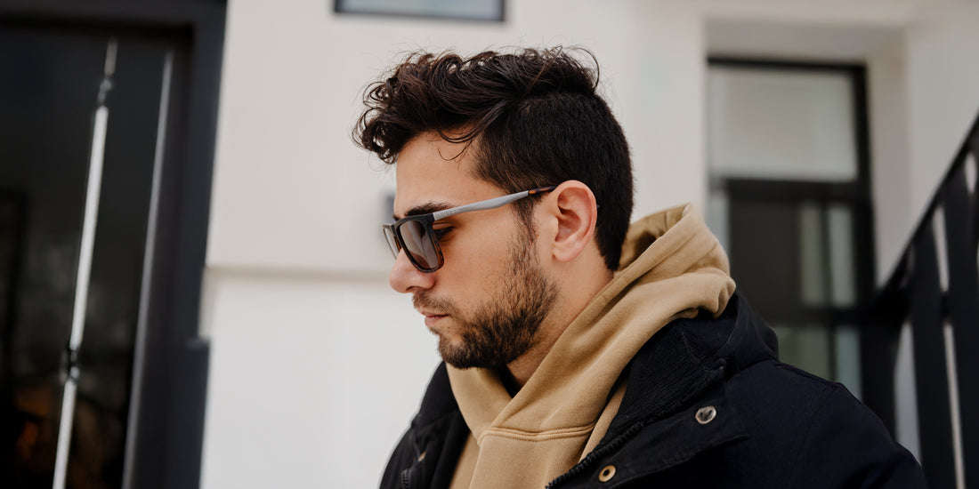 Man wearing tortoiseshell Repeater sunglasses looking down on a city street, wearing tan hoodie and black jacket