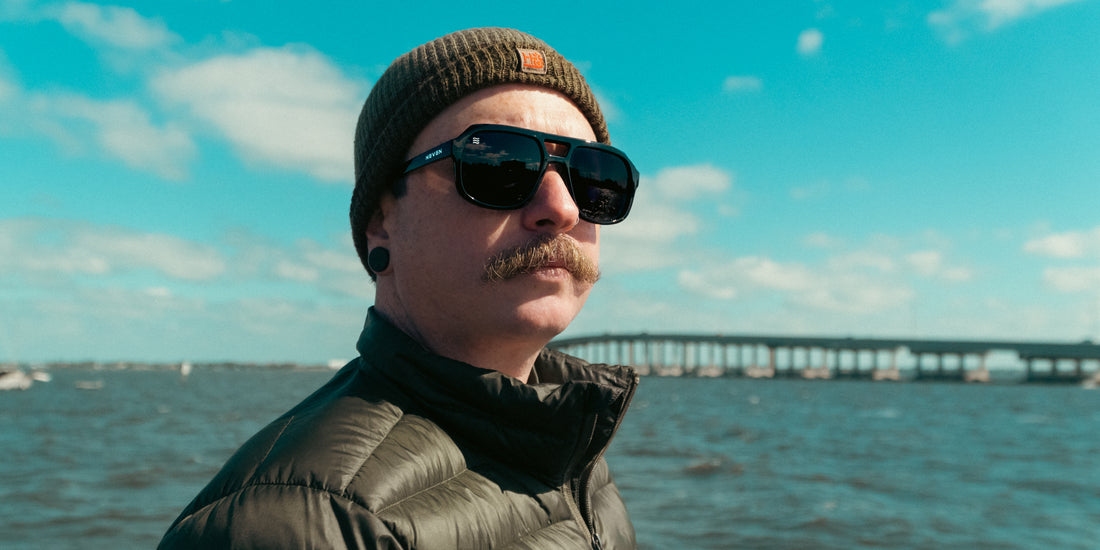 Three-quarter view of Cosmo aviator sunglasses on a man showing black glossy frames and polarized lenses reflecting a bridge