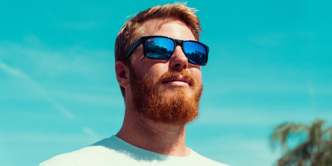Man wearing Blue Steel XL sunglasses with glossy black frame and blue polarized lenses looking toward a bright blue sky