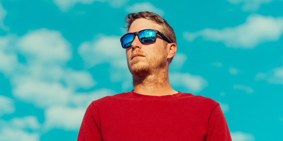 Man wearing Blue Steel sunglasses looking upward in a red shirt against a blue sky
