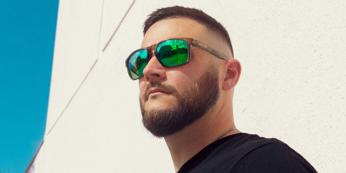 Man wearing Stormy transparent gray polarized sunglasses with green lenses looking up by a white wall and blue sky