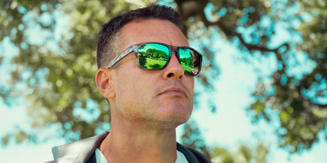 Close-up of Stormy sunglasses on a man showcasing transparent gray gloss TR90 frame and green polarized lenses with blurred trees behind
