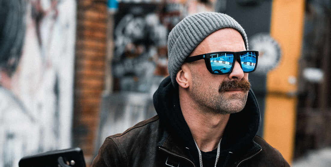 Man wearing Honest John’s sunglasses with matte black frames and blue polarized lenses in an urban outdoor setting