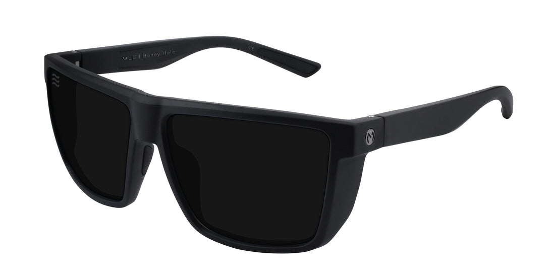 Angled close-up of Honey Hole sunglasses showing matte black rectangular frame, JM logo on temple and black lenses on white background