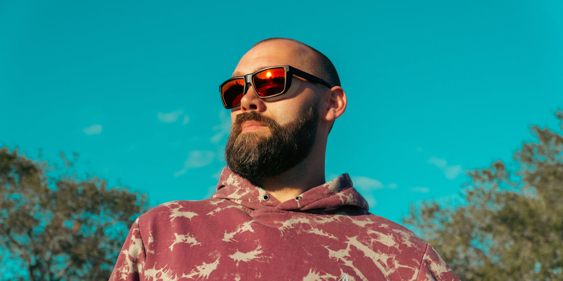 Bearded man wearing Long Point red polarized sunglasses outdoors against a bright blue sky