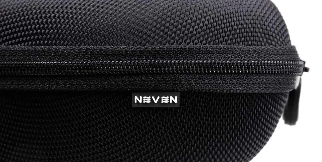 Close-up of Signature Hard Case showing zippered top, textured black polyester surface, and Neven tilde logo tag on white background