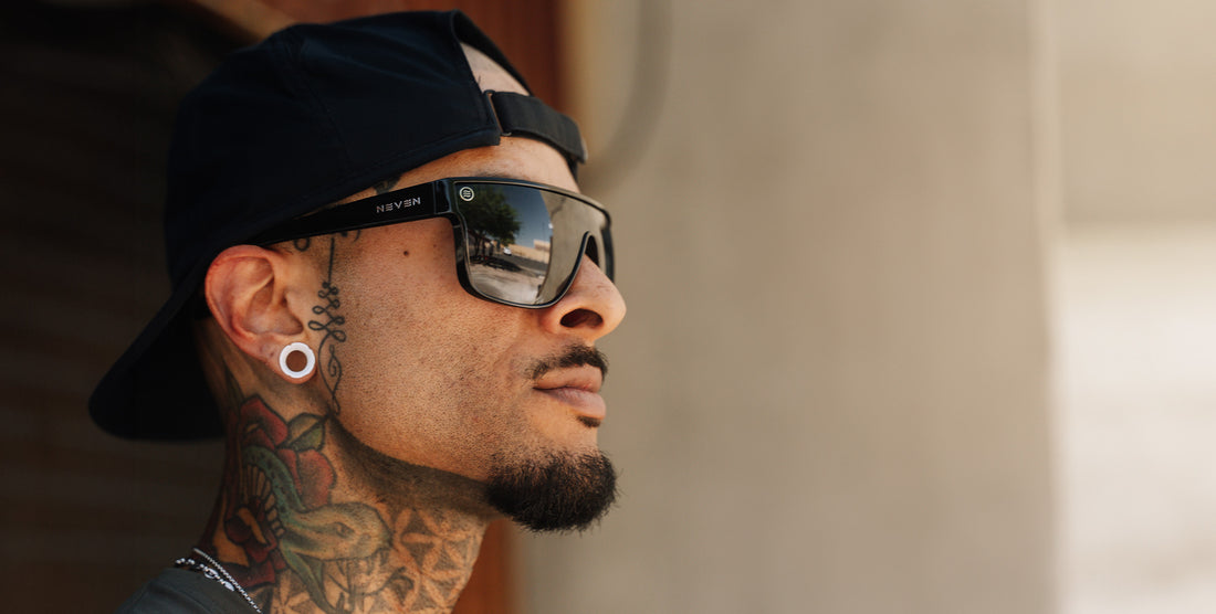 Side view of Wire sunglasses showing black shield polarized lenses, glossy black frame and NEVEN logo on the temple, worn by a tattooed model