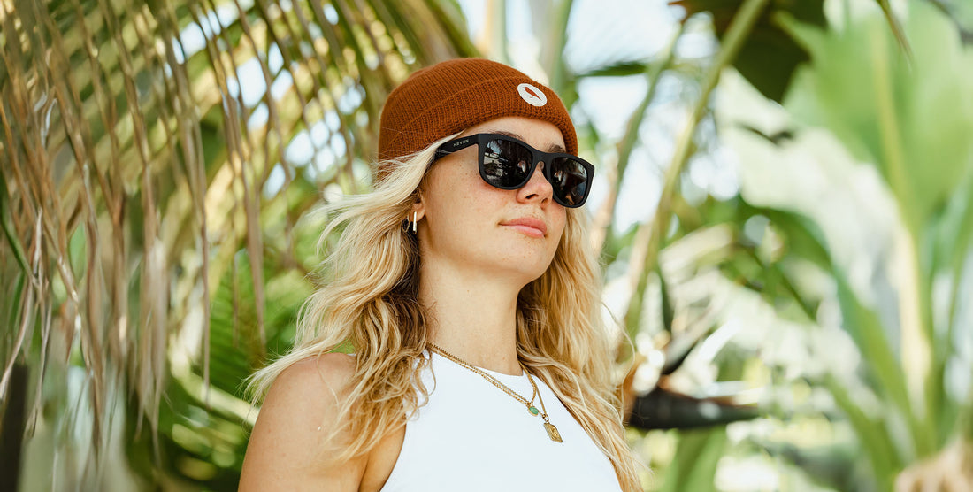 Woman wearing black Classic polarized sunglasses and a brown cap outdoors among tropical greenery