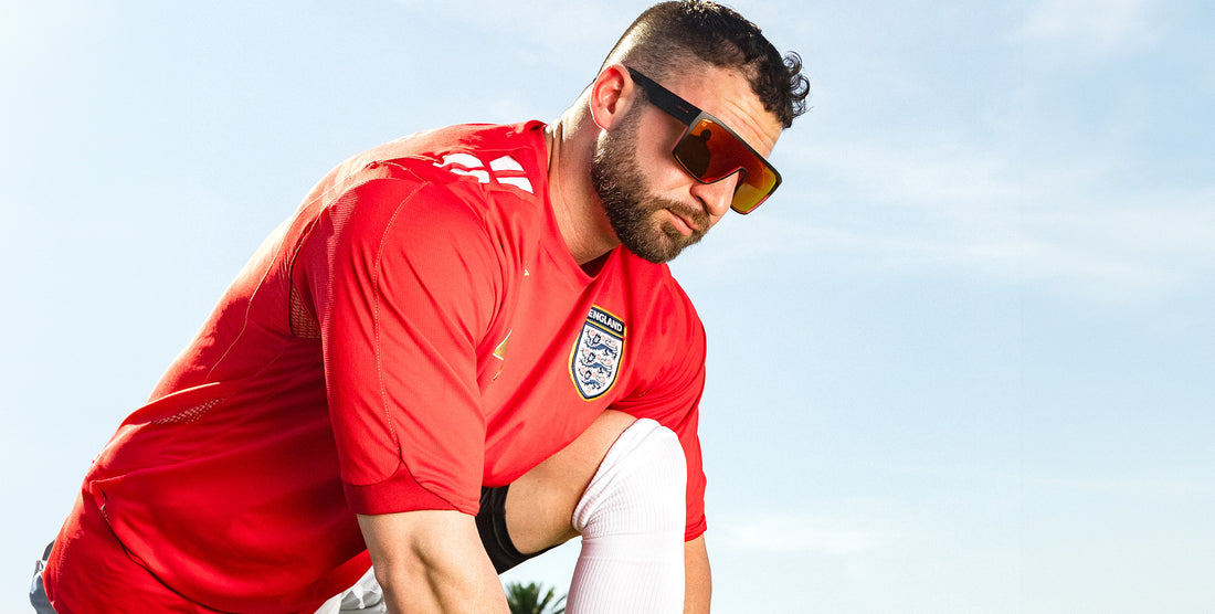 Man crouching wearing black and red 2nd Light wraparound polarized sunglasses with red orange lenses against blue sky