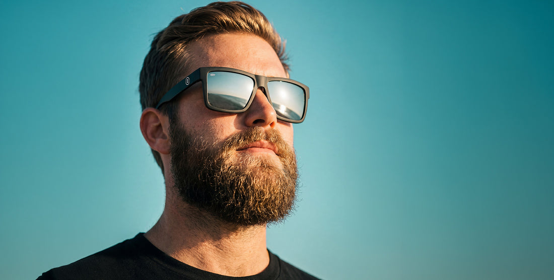 Close-up of Ace XL sunglasses showing matte black oversized frame with silver mirrored lenses against teal sky
