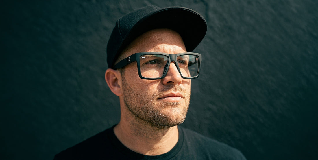 Close-up of Malibu XL glasses showing oversized matte black TR90 rectangular frame with clear lenses against a dark wall