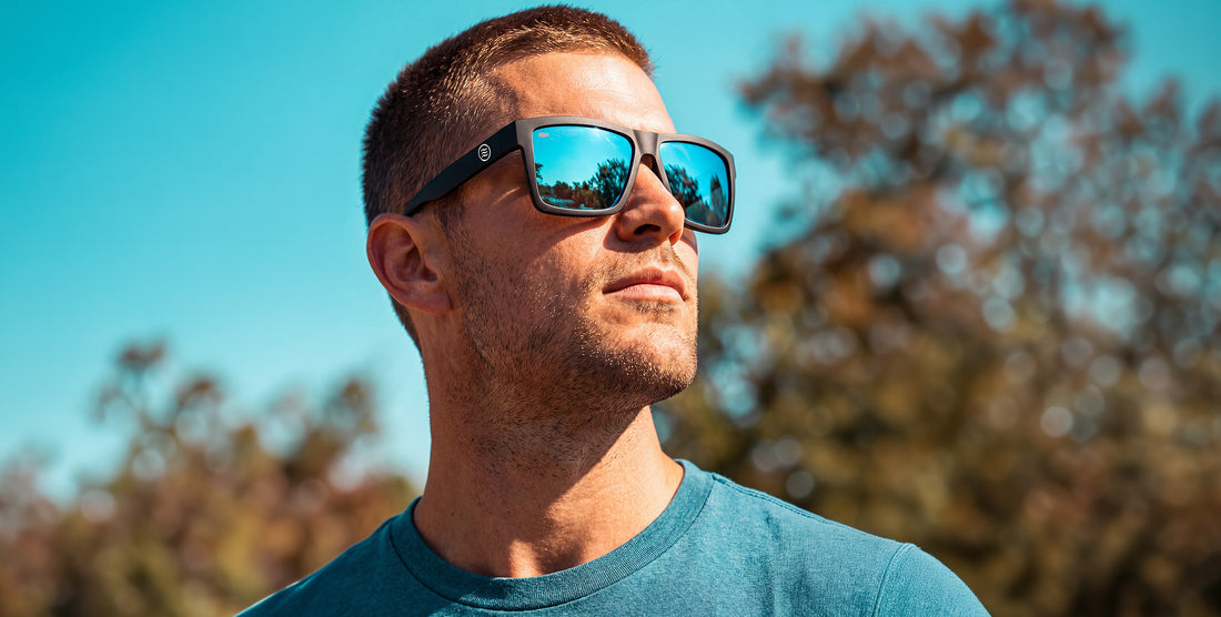 Close up of Montauk XL sunglasses showcasing matte black frame and mirrored blue polarized lenses against blue sky