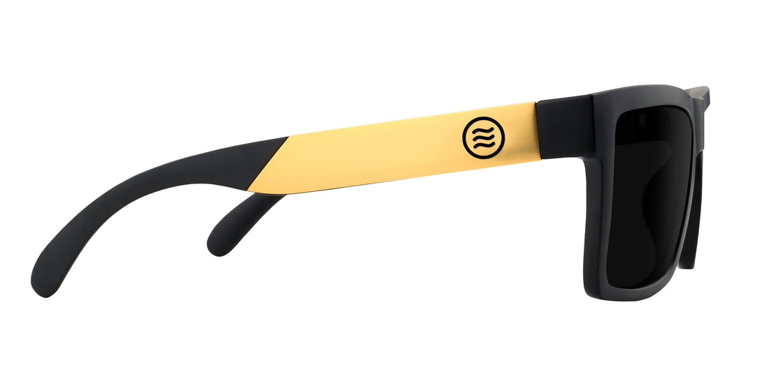 Side view of Prospector XL sunglasses showcasing black matte frame and gold metal temple with circular logo on white background